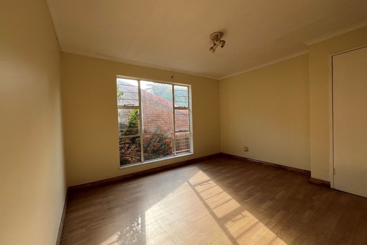 A vacant bedroom featuring laminate wood flooring, neutral walls, and a large window providing natural light.