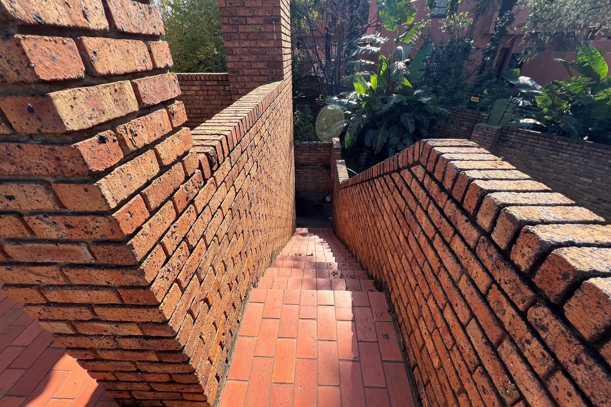 An outdoor staircase featuring exposed face brick walls and terracotta tiled steps, leading down into a landscaped garden area.