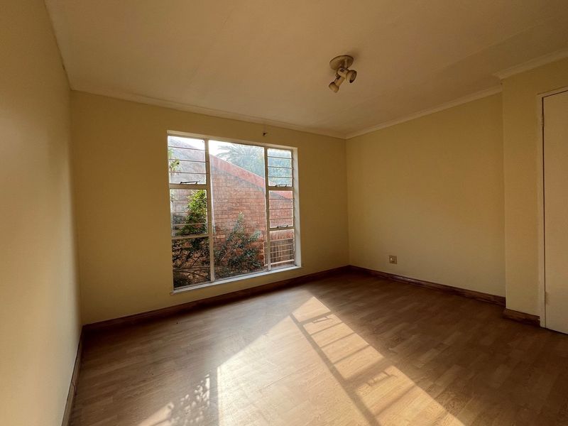 A vacant bedroom featuring laminate wood flooring, neutral walls, and a large window providing natural light.