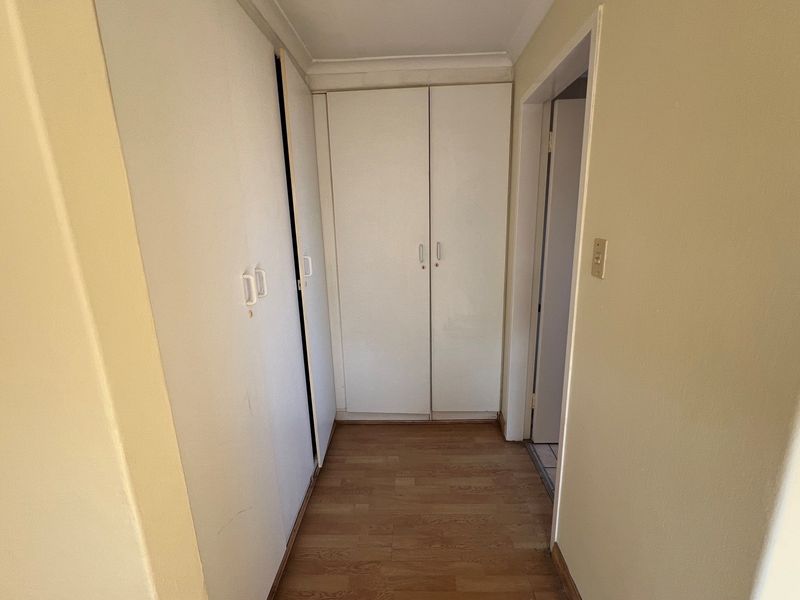 A functional hallway featuring built-in storage cupboards with white doors and wood-look laminate flooring.