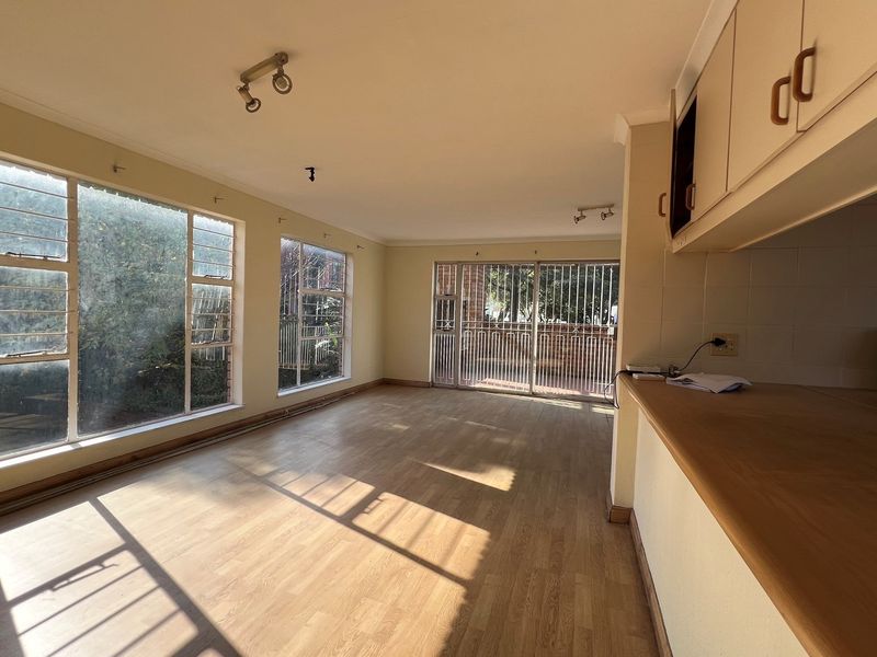 An open-plan living area featuring wood-look flooring, large windows, and a breakfast counter connecting to the kitchen space.