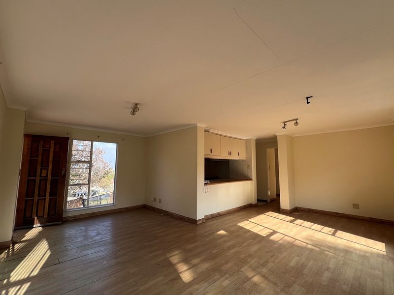 Spacious open-plan living area featuring wood-look flooring, large windows for natural light, and a built-in kitchen serving hatch with overhead cabinetry.