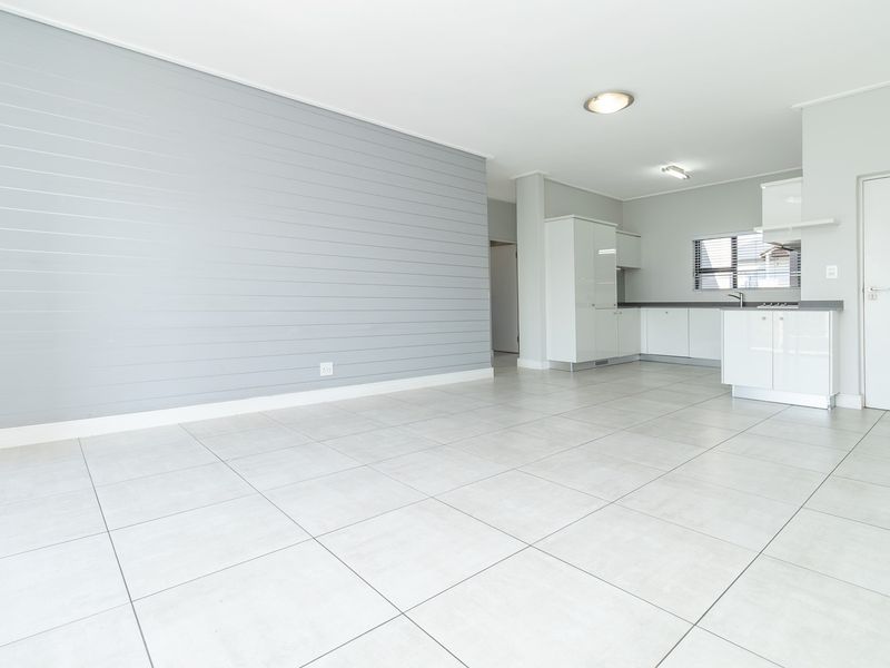 Bright open-plan living area featuring modern tiled flooring, a stylish grey shiplap feature wall, and a clean, contemporary kitchen with white cabinetry.