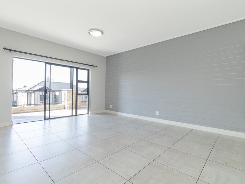 A bright, empty living room featuring large format floor tiles, a grey shiplap feature wall, and sliding glass doors leading to an outdoor balcony.