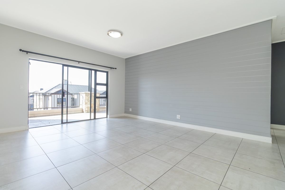 A bright, empty living room featuring large format floor tiles, a grey shiplap feature wall, and sliding glass doors leading to an outdoor balcony.