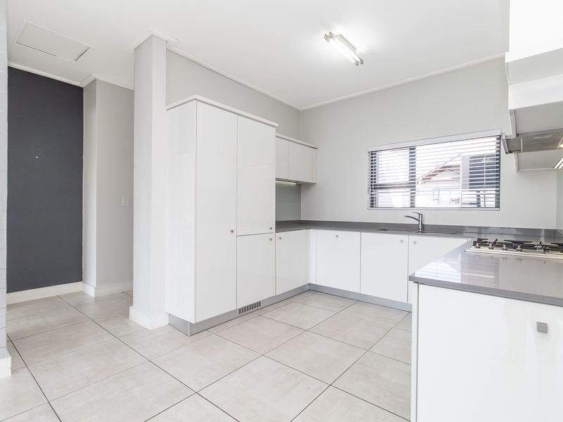 Modern kitchen featuring white high-gloss cabinetry, stone countertops, a gas hob with extractor, and neutral tiled flooring in a clean, open layout.