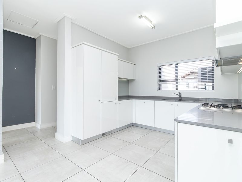 Modern kitchen featuring white cabinetry, stone countertops, a gas hob, extractor fan, and neutral tiled flooring in a clean, well-lit space.