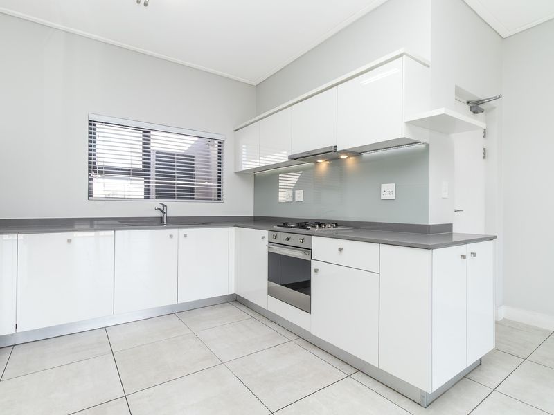 Modern kitchen featuring sleek white cabinetry, stone countertops, integrated stainless steel appliances, and a glass splashback, finished with neutral floor tiles.