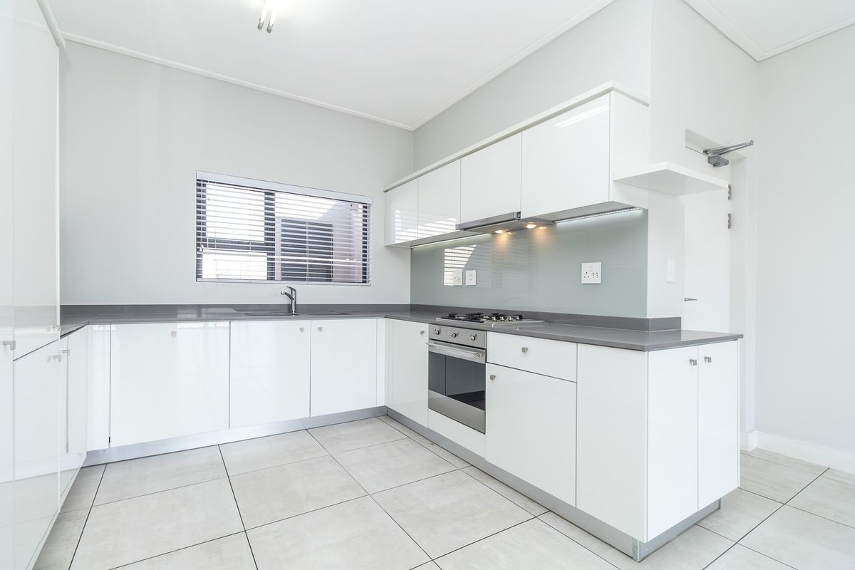 Modern kitchen featuring white high-gloss cabinetry, stone countertops, integrated stainless steel appliances, and neutral tiled flooring in a clean, minimalist layout.