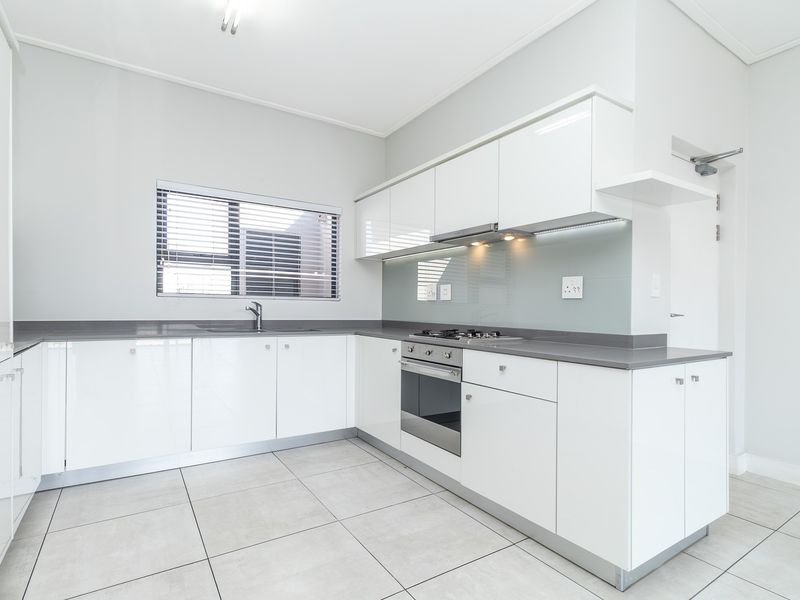 Modern kitchen featuring white high-gloss cabinetry, stone countertops, integrated stainless steel appliances, and neutral tiled flooring in a clean, minimalist layout.