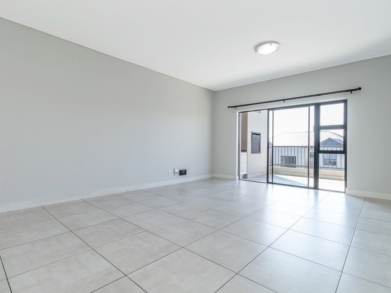A bright, empty living room featuring neutral tiled flooring and a large sliding glass door providing access to an outdoor balcony area.
