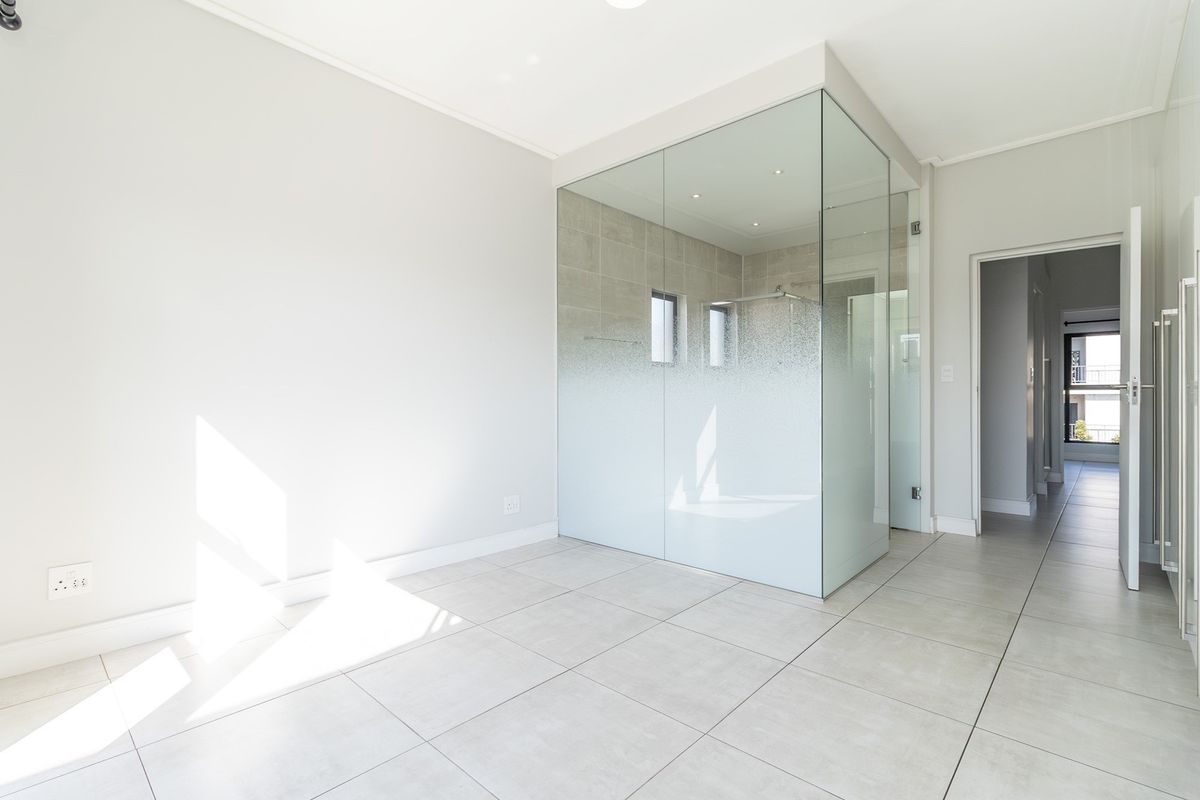 Modern bedroom featuring a sleek glass-enclosed en-suite bathroom with frosted privacy detailing and neutral tiled flooring throughout.