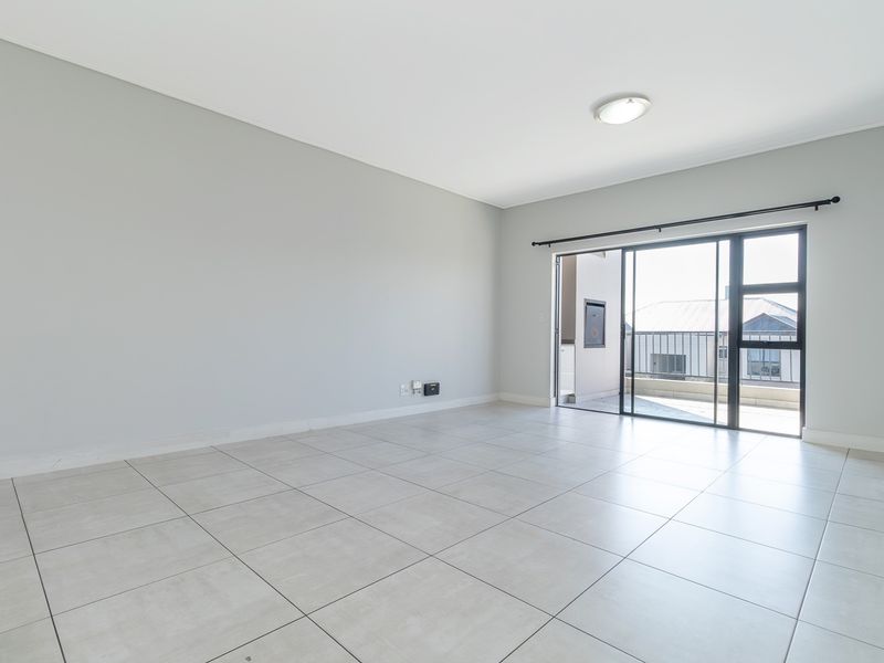 A bright, empty living room featuring neutral tiled flooring and a large sliding glass door providing access to an outdoor balcony area.