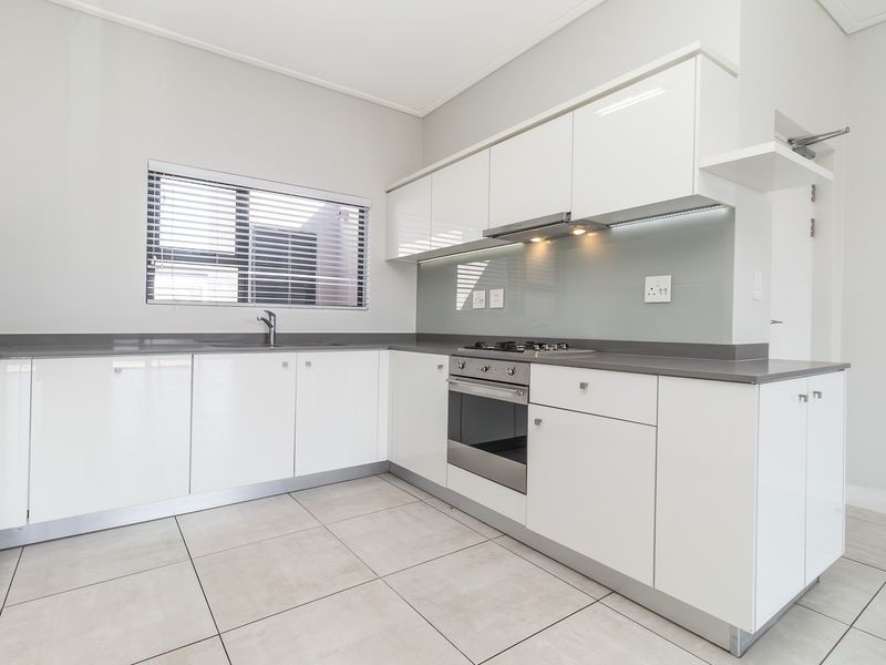 Modern kitchen featuring high-gloss white cabinetry, quartz countertops, glass splashback, and integrated stainless steel appliances with neutral tiled flooring.