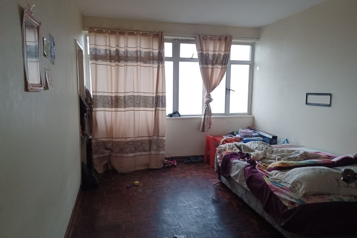 A bedroom featuring parquet flooring and a large window with natural light, providing a functional space for rest.