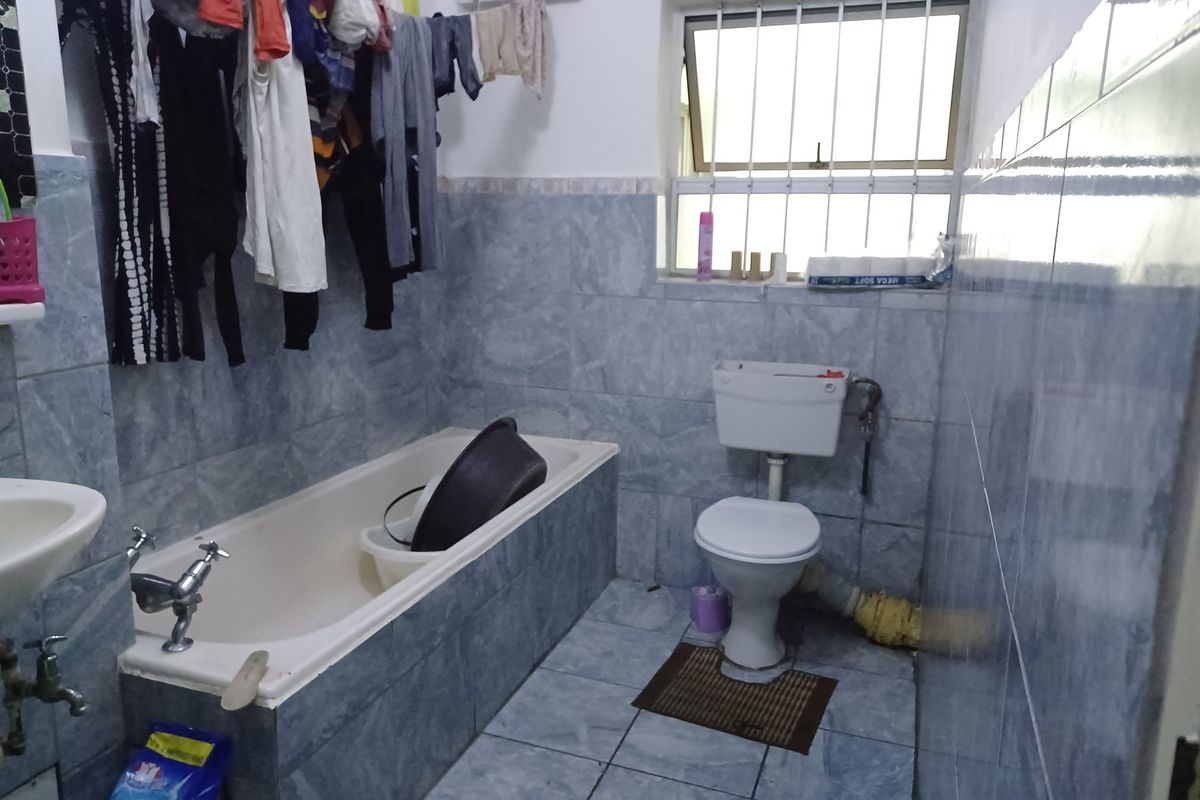 A functional bathroom featuring a bathtub, toilet, and basin with tiled walls and floors, including a window with security bars.
