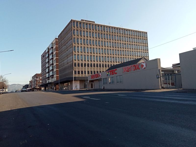 Street level view of a multi-story commercial building and adjacent office premises in an urban setting.