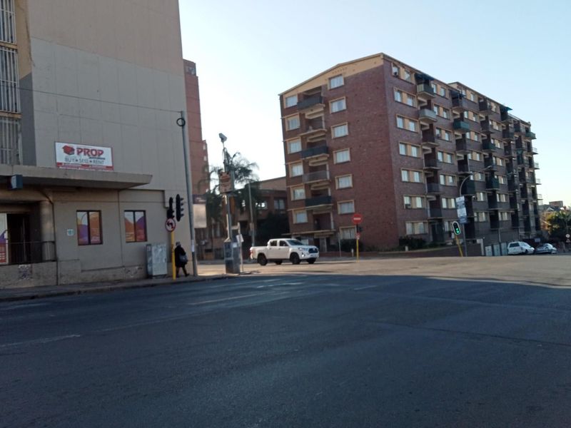 A street-level view of a city intersection featuring a multi-story brick apartment building and surrounding urban infrastructure.