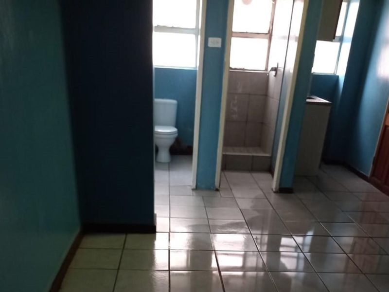 A functional bathroom featuring tiled flooring, a standard toilet, and a shower cubicle, currently presenting in a dated condition.
