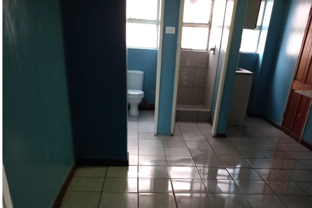A functional bathroom featuring tiled flooring, a standard toilet, and a shower cubicle, currently presenting in a dated condition.
