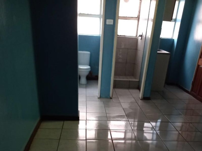 A functional bathroom featuring tiled flooring, a toilet, and a shower cubicle, currently in need of cosmetic updates to improve its overall condition.