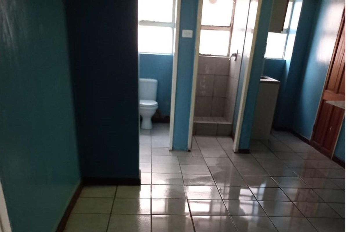 A functional bathroom featuring tiled flooring, a toilet, and a shower cubicle, currently in need of cosmetic updates to improve its overall condition.