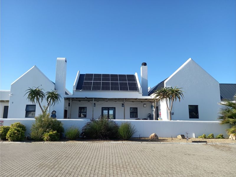 A well-maintained single-story residence featuring a white facade, dual chimneys, and a roof-mounted solar panel array, set behind a low boundary wall.