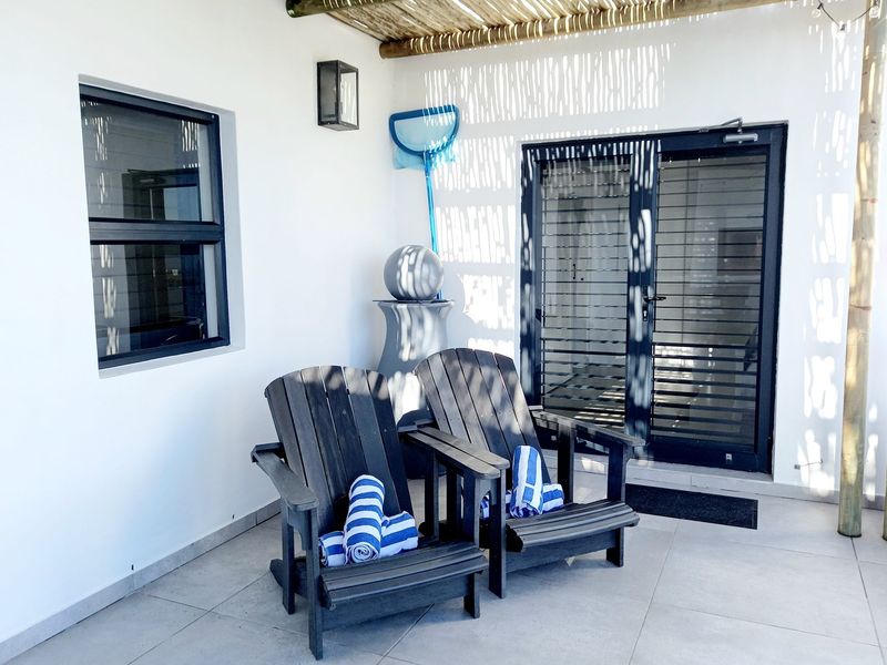 A covered patio area featuring tiled flooring, a timber pergola roof structure, and modern dark-framed glass sliding doors leading into the home.