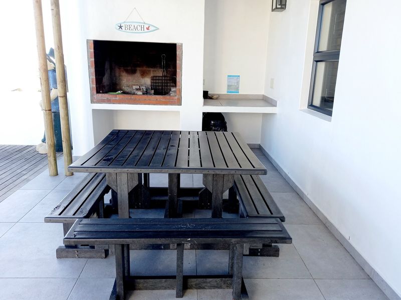 Covered patio area featuring a built-in brick fireplace and tiled flooring, providing a functional space for outdoor dining and entertainment.