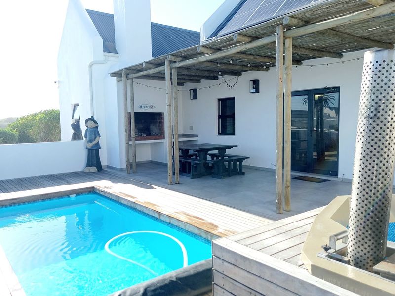 Outdoor entertainment area featuring a swimming pool, wooden decking, and a covered patio with a built-in braai, perfect for relaxed alfresco dining.