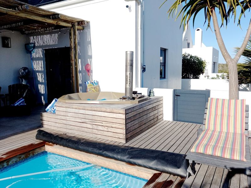 Outdoor pool area featuring a built-in hot tub with wood cladding, timber decking, and a covered patio space.