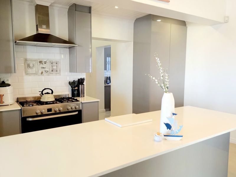 Modern kitchen featuring a central island, sleek grey cabinetry, subway tile backsplash, and a stainless steel gas range with an extractor fan.
