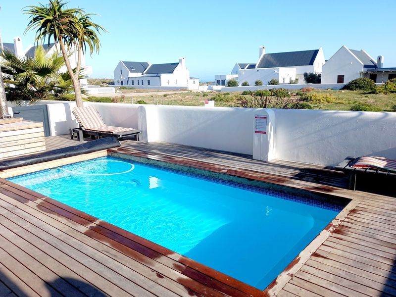 Outdoor pool area featuring a rectangular swimming pool surrounded by timber decking and a low white boundary wall with views of the estate.