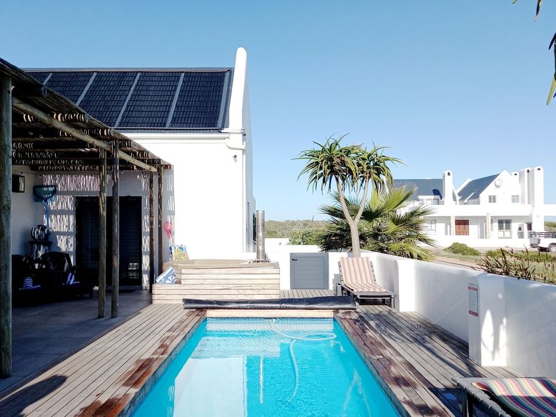 Outdoor pool area featuring a wooden deck, a built-in hot tub, and a covered patio area with solar panels installed on the roof.