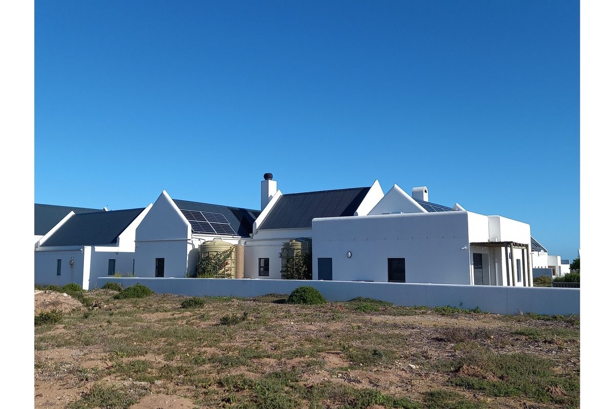 A rear view of a modern white house featuring a pitched roof, solar panels, and integrated water storage tanks.