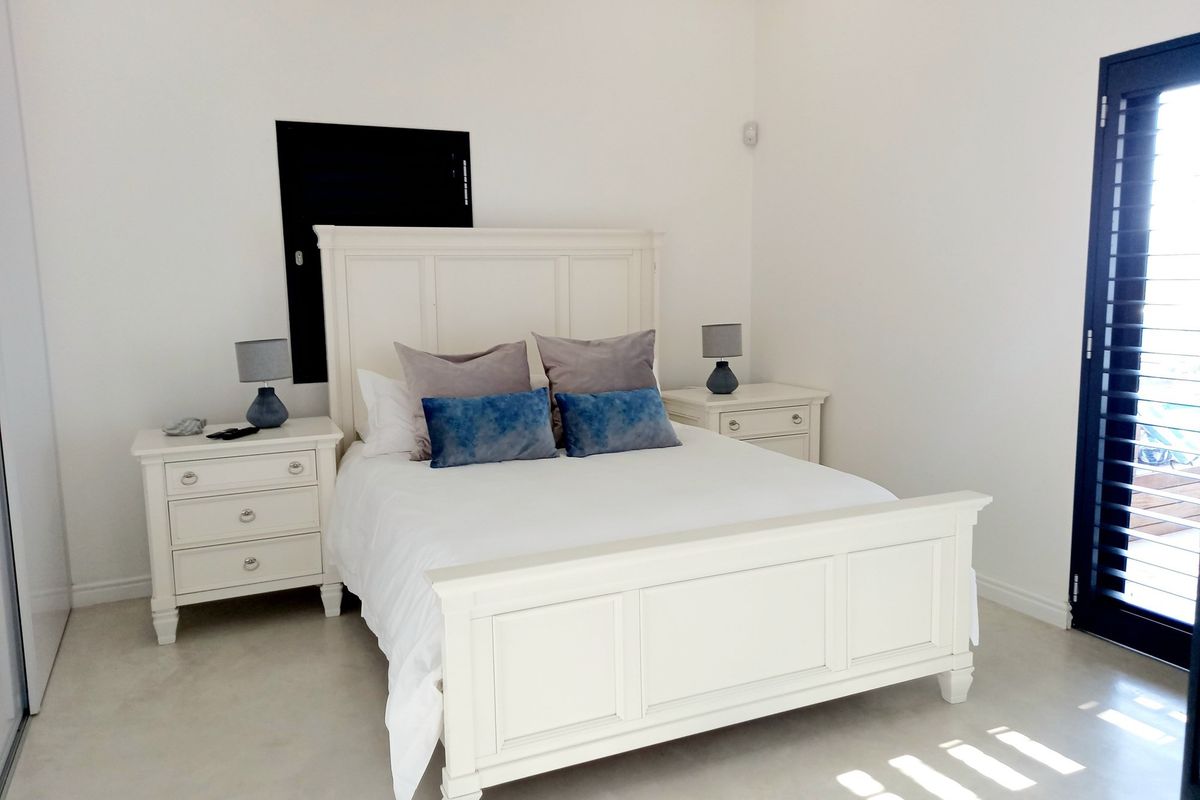 A bright bedroom featuring neutral tiled flooring, white walls, and a dark-framed glass door leading to an outdoor area.
