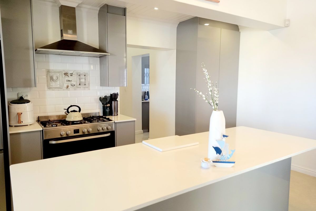 Modern kitchen featuring a central island, sleek grey cabinetry, subway tile backsplash, and a stainless steel gas range with an extractor fan.