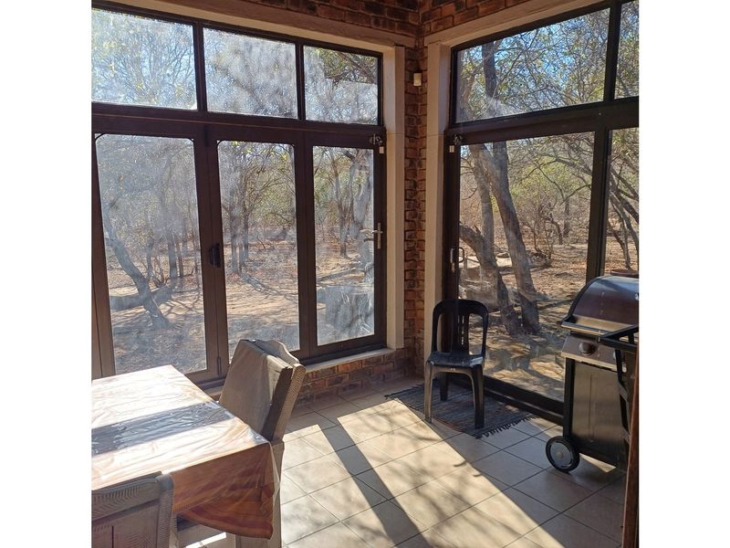A sunlit enclosed patio featuring exposed brick walls, large windows with natural views, and tiled flooring, perfect for relaxed indoor-outdoor living.