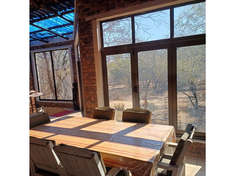 A covered patio area featuring exposed brick walls, large glass doors, and a translucent roof, offering views of the surrounding natural landscape.
