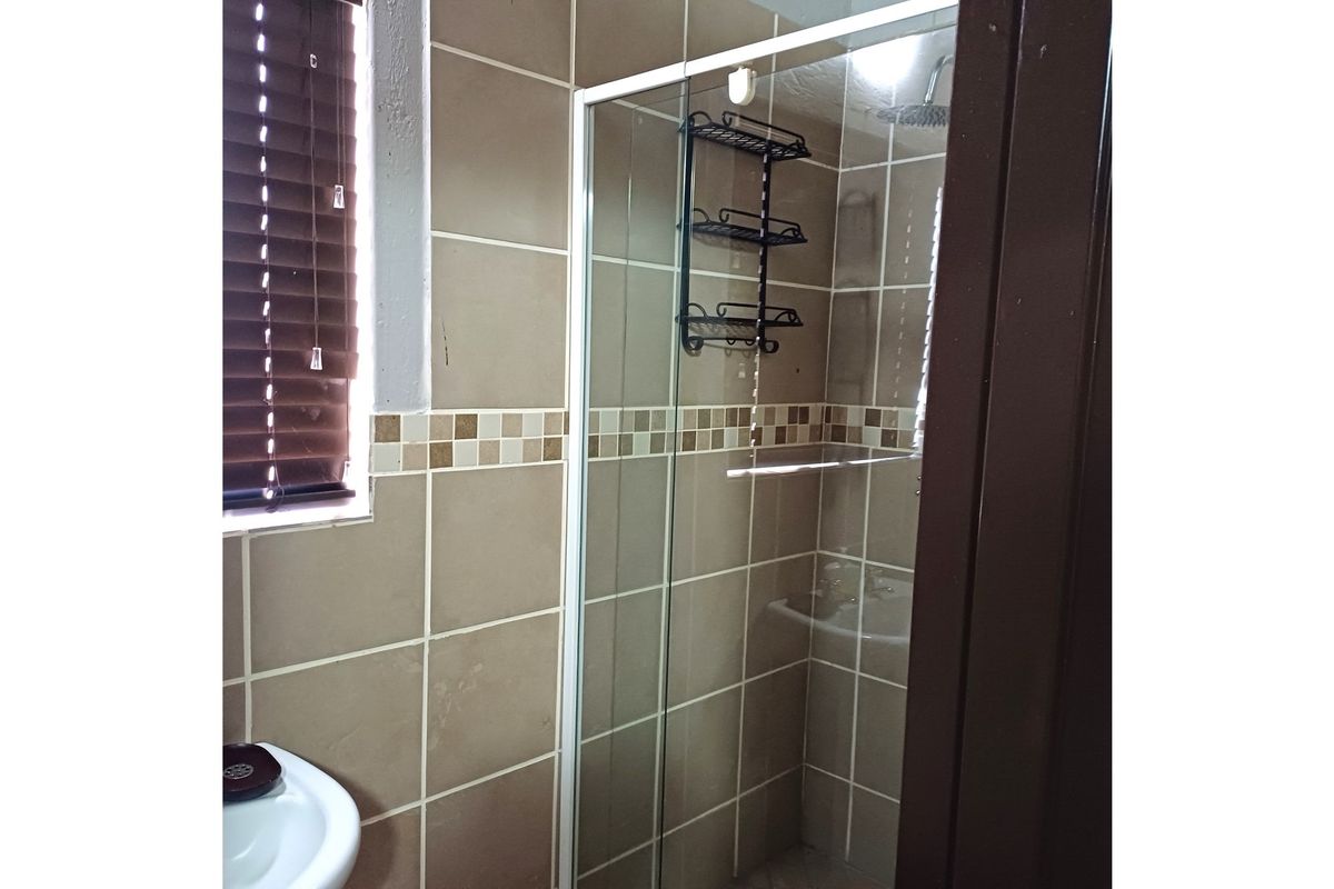 A functional bathroom featuring a glass-enclosed shower, tiled walls with decorative accents, and a pedestal basin.