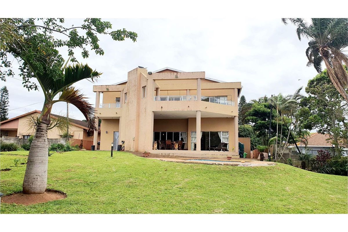 Rear view of a multi-story house featuring a covered patio, upper-level balcony, swimming pool, and a spacious landscaped garden.
