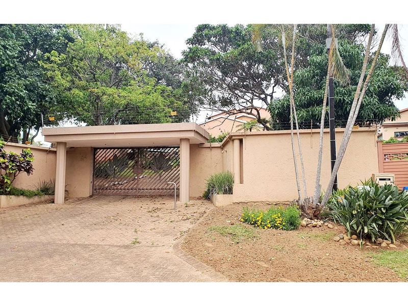 Front entrance view featuring a paved driveway, perimeter wall with electric fencing, and a secure metal gate.