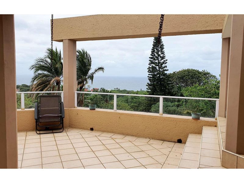 Covered balcony featuring tiled flooring, glass balustrades, and elevated views of the surrounding landscape and ocean.