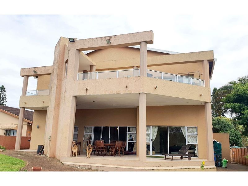 Rear elevation of a multi-level house featuring a covered patio, upper-level balconies with glass balustrades, and large sliding glass doors.