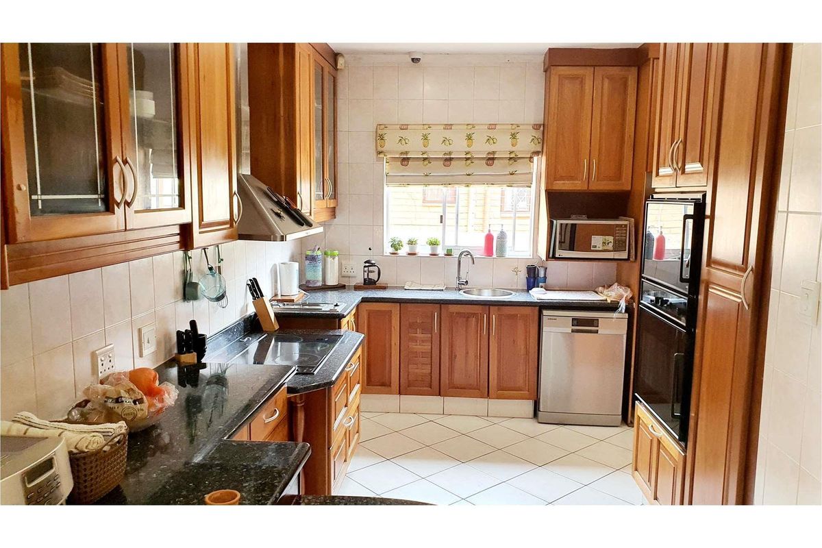 A functional kitchen featuring traditional wooden cabinetry, granite countertops, built-in oven, extractor fan, and tiled finishes throughout.