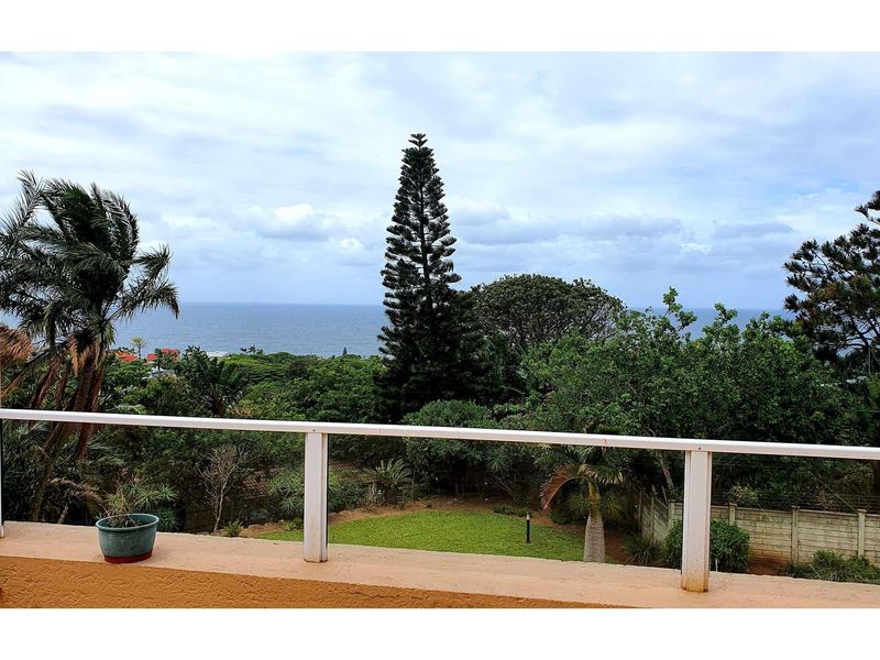 Elevated balcony view overlooking a lush garden with mature trees and a distant ocean horizon.