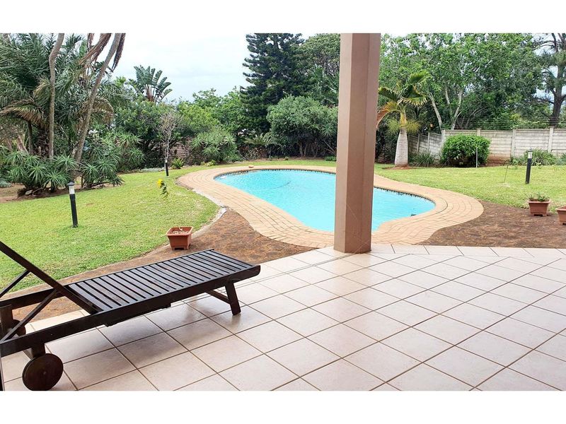 A covered tiled patio overlooking a swimming pool and a spacious garden area with established landscaping.