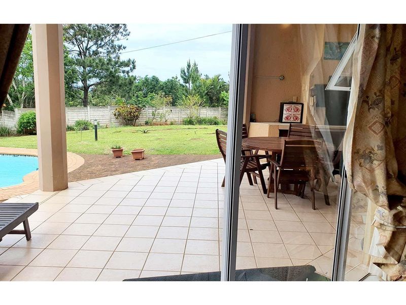 Covered patio area featuring tiled flooring and a built-in braai, overlooking a private garden and swimming pool.