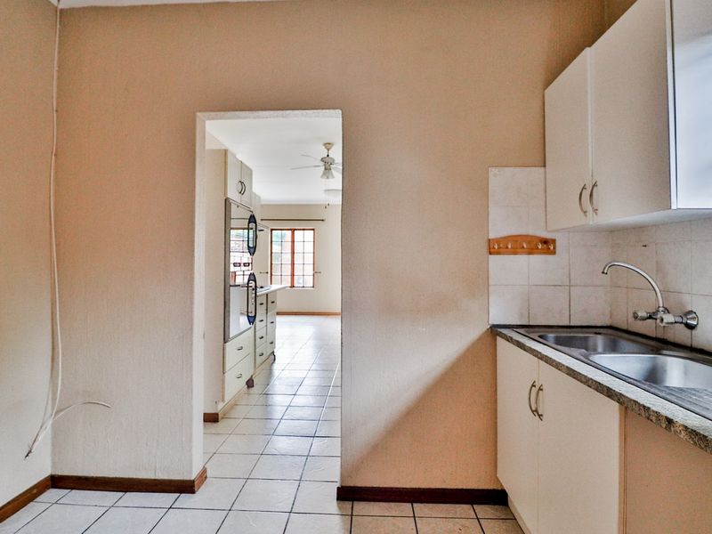 A functional kitchen area featuring tiled flooring, built-in cabinetry, and a double bowl sink, with an open doorway leading to an adjacent living space.