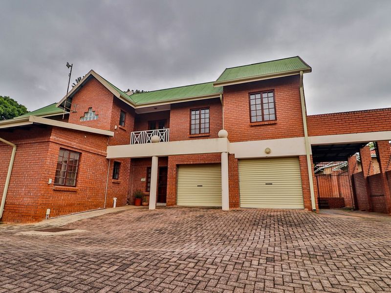 A double-story brick house featuring a double garage with roller shutter doors, a paved driveway, and an upper-level balcony.